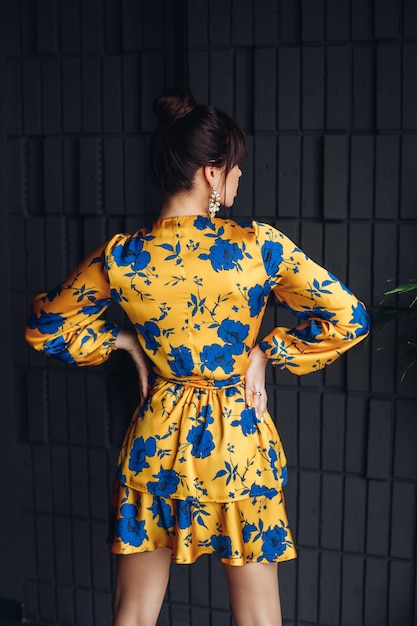 Picture of young lovely caucasian female with dark hair in yellow and blue dress, gold shoes shows different poses for the camera