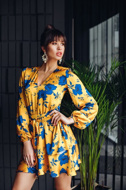 Picture of young lovely caucasian female with dark hair in yellow and blue dress, gold shoes shows different poses for the camera