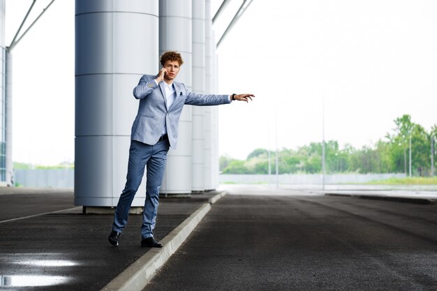 Picture of young redhaired businessman catching the car and talking on phone