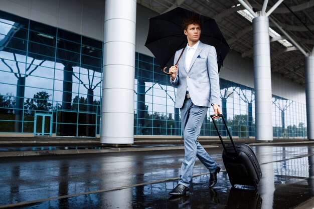 黒い傘と空港で雨の中歩いてスーツケースを保持していると兄弟分青年実業家の画像