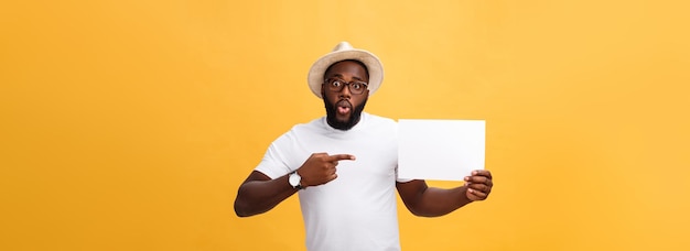 Free photo picture of young smiling africanamerican man holding white blank board and pointing on it on yellow