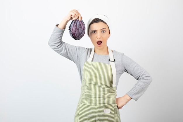 Picture of young surprised housewife showing purple cabbage on white 