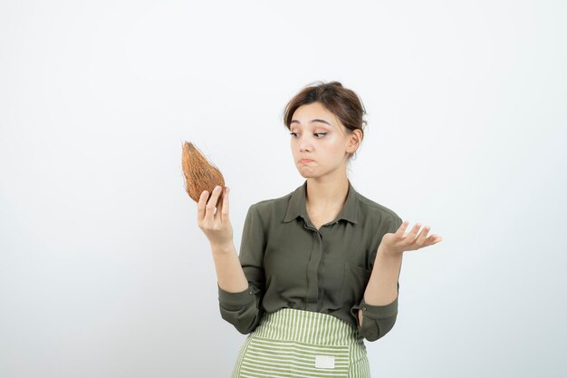 白い壁にココナッツを持っているエプロンの若い女性の写真。高品質の写真
