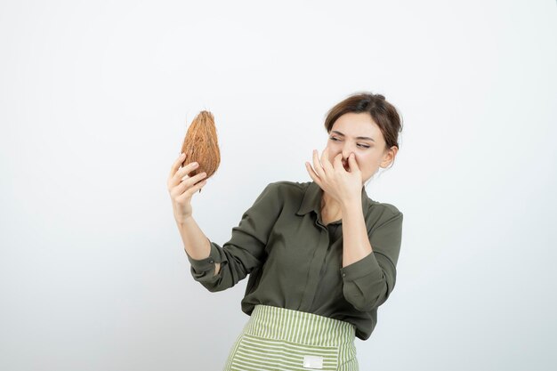 Picture of young woman in apron holding a coconut and covering nose . High quality photo