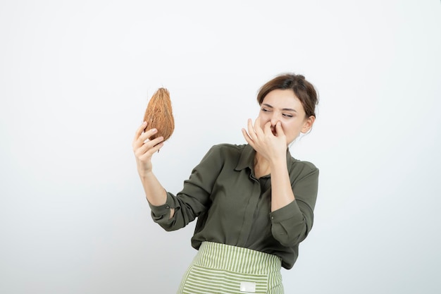 코코넛을 들고 코를 덮고 앞치마를 입은 젊은 여성의 사진. 고품질 사진