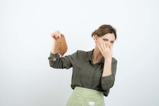 Picture of young woman in apron holding a coconut and covering nose . High quality photo