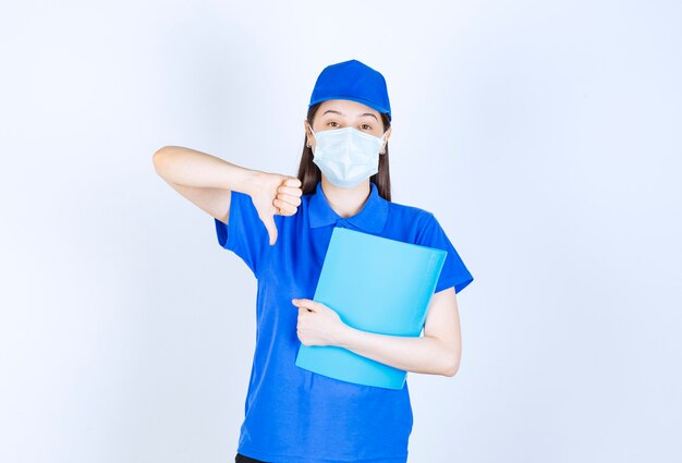 Picture of young woman in cap and uniform holding folder and showing thumb down. 