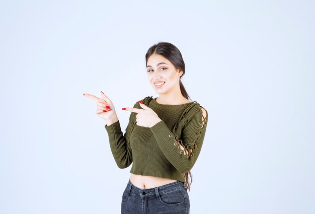 Picture of a young woman model standing and pointing aside with index finger