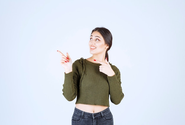 Изображение модели молодой женщины, стоящей и указывающей в сторону указательным пальцем