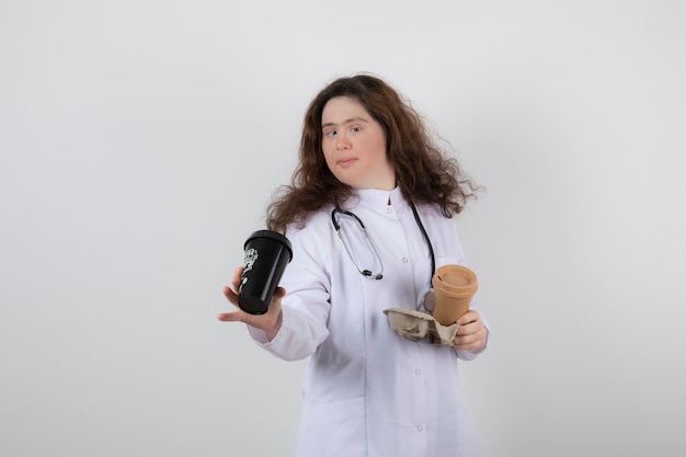 Picture of a young woman model in white uniform holding a cardboard with cups of coffee.