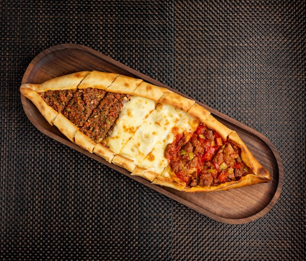 Pide with stuffed meat cheese and pieces of fried meat on a wooden bowl