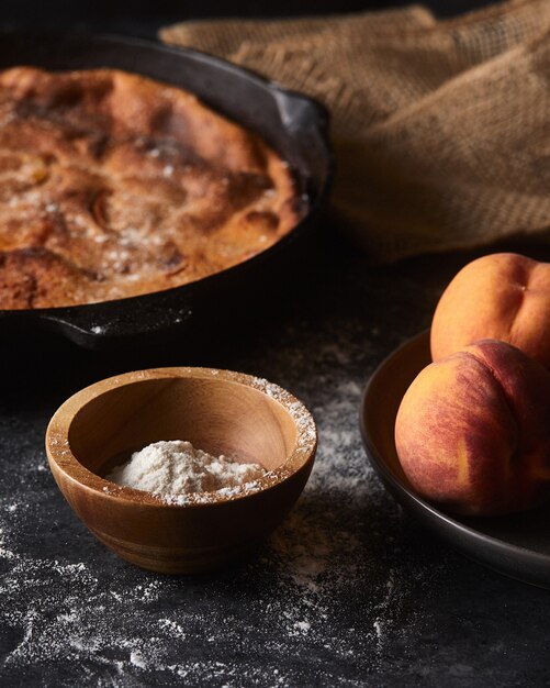 pie and a bowl of peaches on a black surface covered with flour