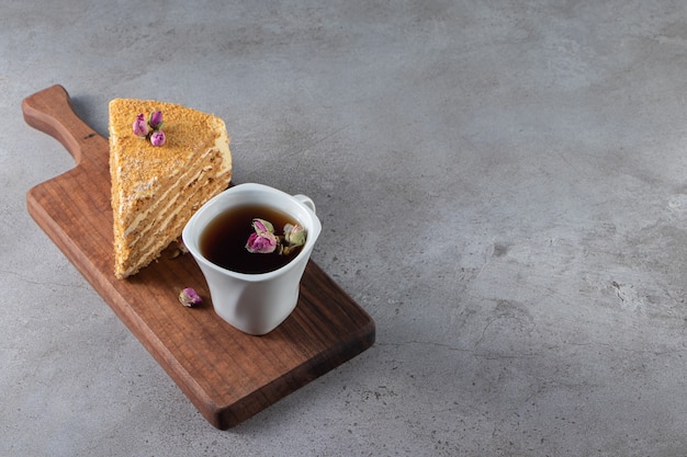 Piece of cake napoleon next to a cup of tea on a cutting board , on the marble table.