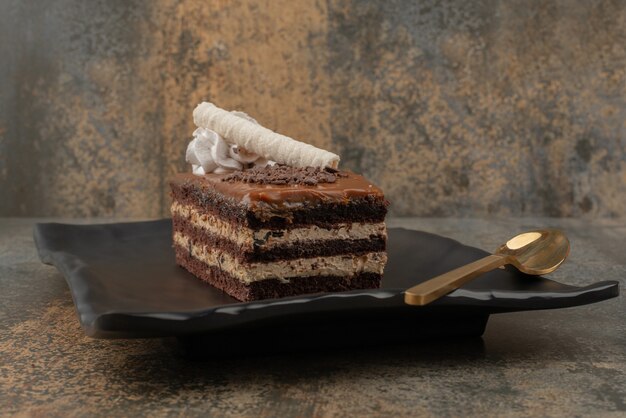 A piece of cake with golden spoon on dark plate