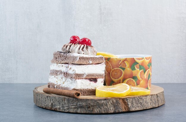 A piece of cake with sliced lemon and cinnamon stick on wooden board