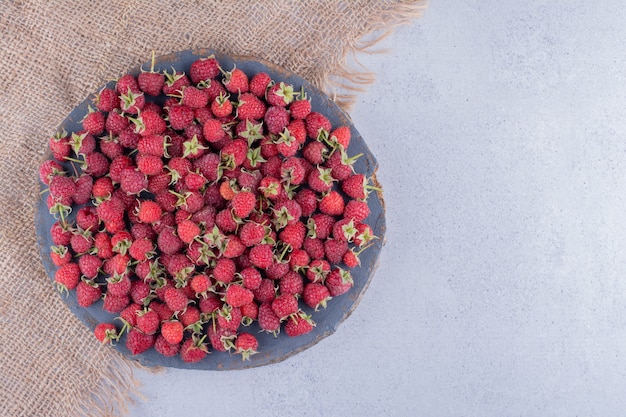 Piece of cloth under a pile of raspberries on a wooden board on marble background. High quality photo