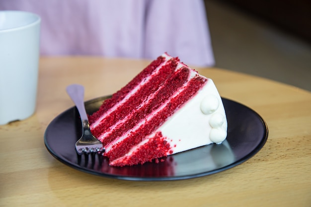 フォークが付いている皿の上のおいしい赤いビロードのケーキの部分。