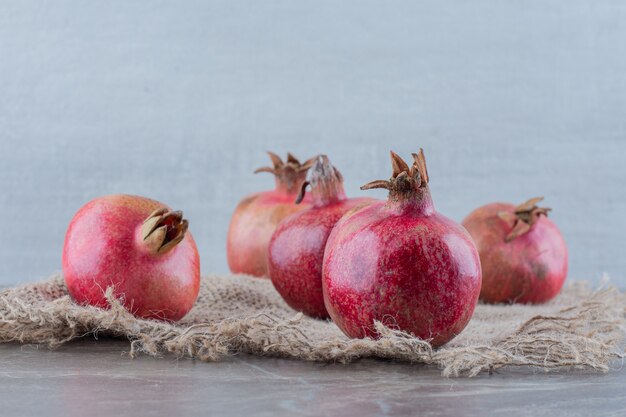 A piece of fabric under a bundle of pomegranantes on marble.