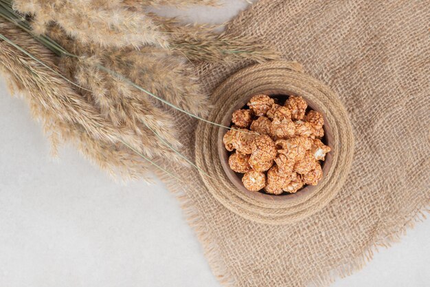 Piece of fabric, trivet, bowl of caramle flavored popcorn and stalks of needlegrass on marble table.