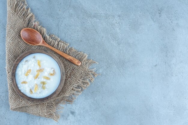 Piece of fabric under a wooden spoon and a bowl of raisin-topped milky rice on marble.