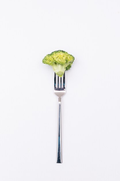 Piece of fresh broccoli on fork isolated on white surface