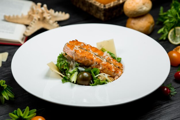 Кусок жареного лосося в белой тарелке с зеленью и пармезаном