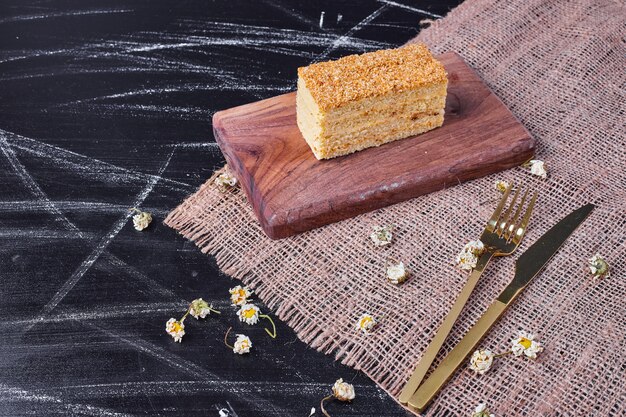 A piece of homemade honey cake on wooden board next to golden cutlery. 
