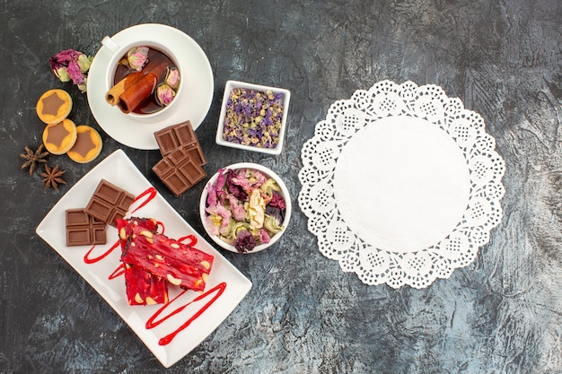 Foto gratuita un pezzo di pizzo con un piatto di cioccolatini e tisane e fiori secchi con biscotti su fondo grigio