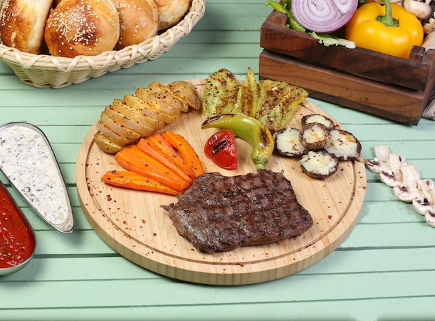 A piece of steak with grilled vegetables on the wooden board.