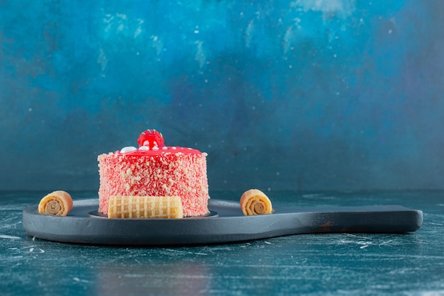 Free photo piece of strawberry cake and waffle rolls on black cutting board.