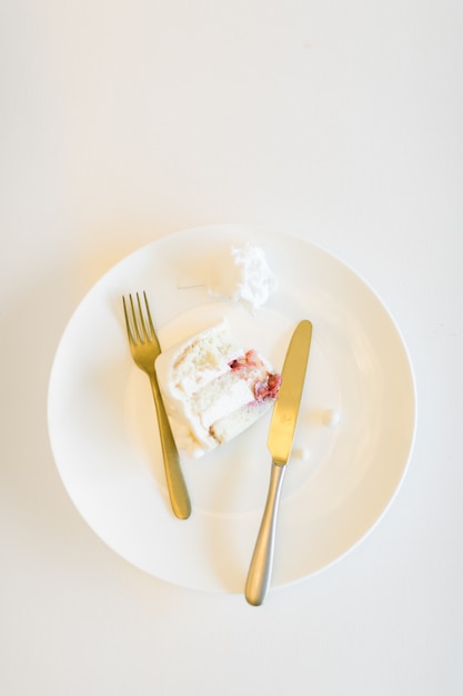 A piece of wedding cake in a white plate with hook and knife top view on a white table background copy space for text