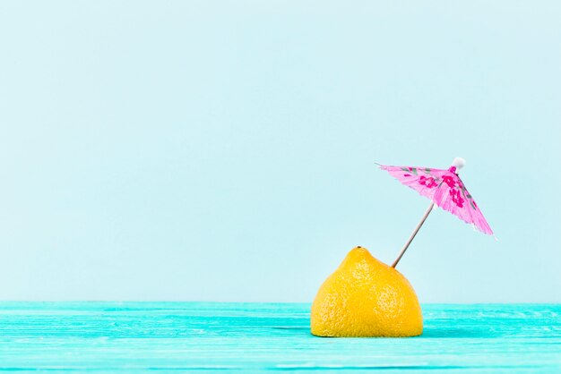 青い背景上にピンクの傘と黄色のレモンの作品