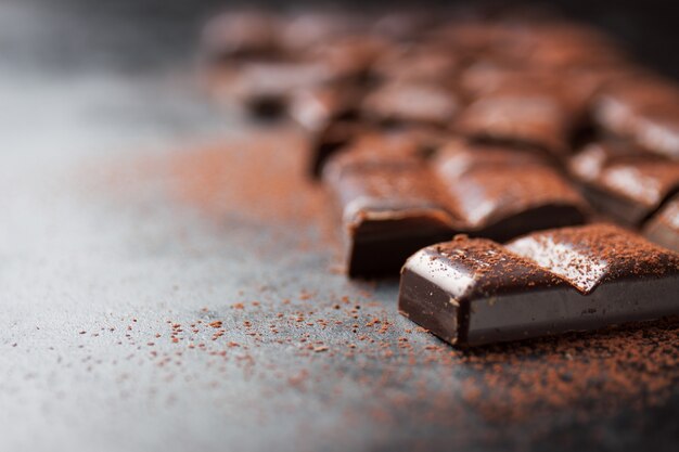 Pieces of chocolate tablet on a black wooden table and cacao sprinkled on top
