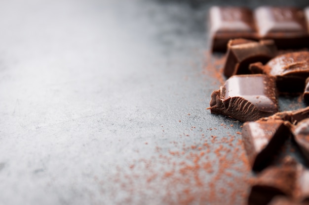 Pieces of chocolate tablet on a black wooden table and cacao sprinkled on top