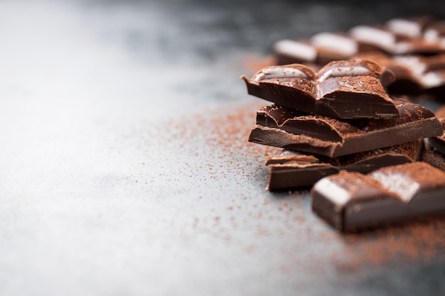 Pezzi di cioccolato su un tavolo in legno e cacao spruzzato