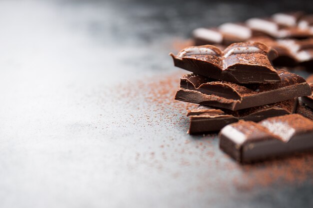 Pieces of chocolate on a wooden table and cacao sprinkled 