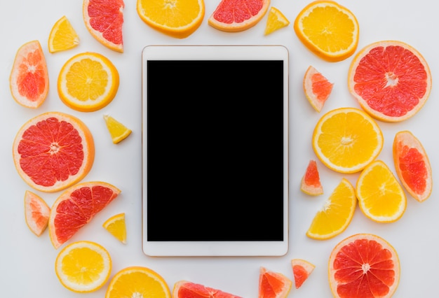 Pieces of citrus fruits around digital tablet