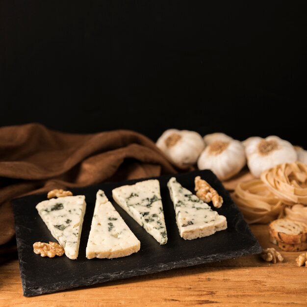 Pieces of gorgonzola cheese on black stone with walnut and garlic over desk