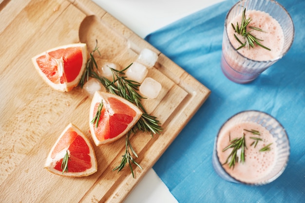 Pieces of grapefruit and rosemary on wooden desk. Healthy detox diet smoothie.Fitness weigth loss concept. From above.