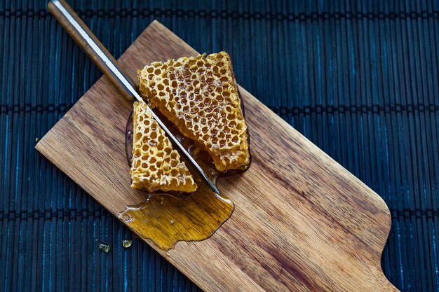 Pieces of honeycomb being cut with knife on wooden chopping board