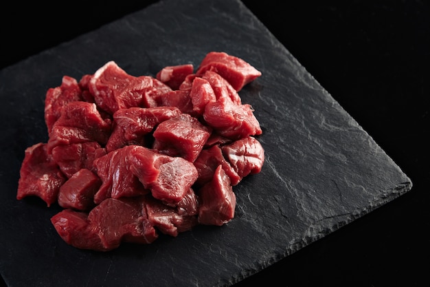 Бесплатное фото Кусочки сырого свежего мяса, изолированные на черной каменной доске сбоку