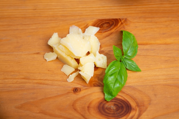 Pieces of parmesan and green basil on wooden table