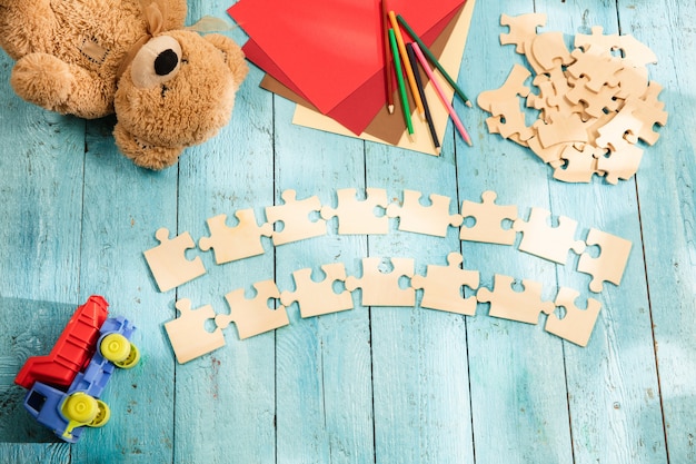 Pieces of puzzles on the surface of wooden table with toys and colors