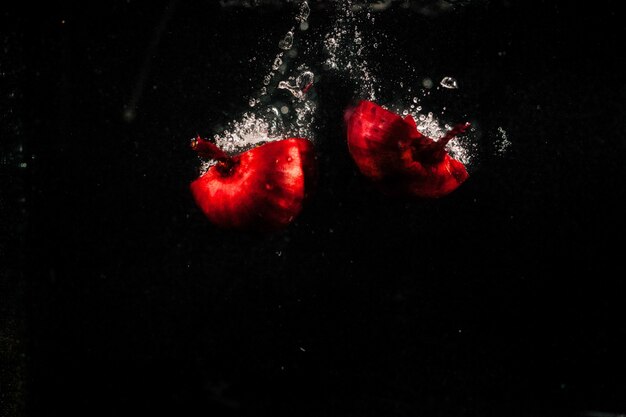 Pieces of red onion fall in water on black background