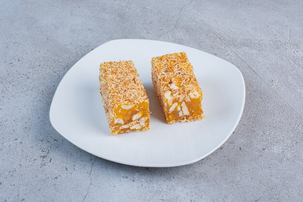 Pieces of Turkish delights coated with sprinkled candy on a white platter on marble background.