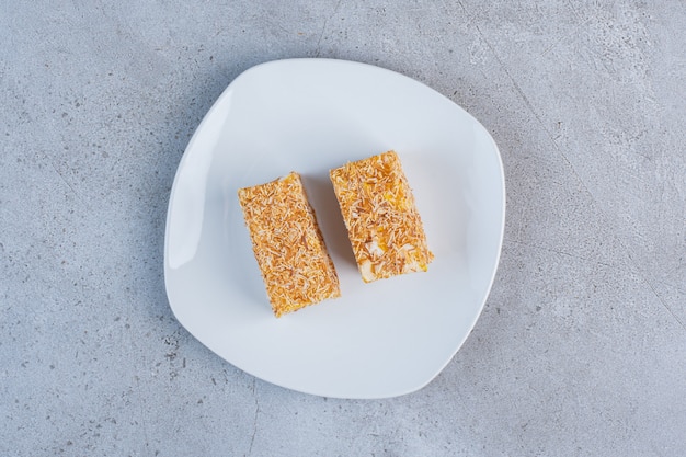 Pieces of Turkish delights coated with sprinkled candy on a white platter on marble background.