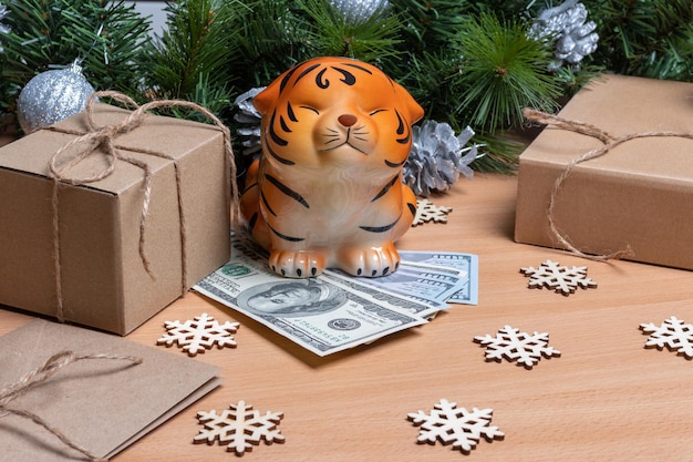 A piggy bank in the shape of a tiger standing on cash dollars on a wooden background with gift boxes, snowflakes and fir branches. success and wealth concept in 2022. year of the tiger concept