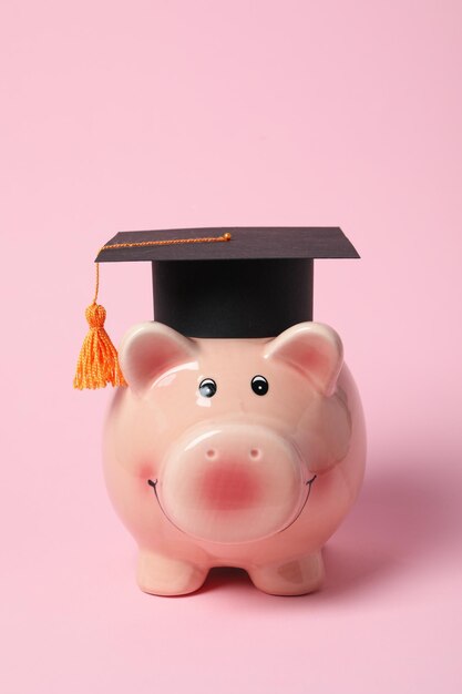 Piggy bank with graduation hat on pink background