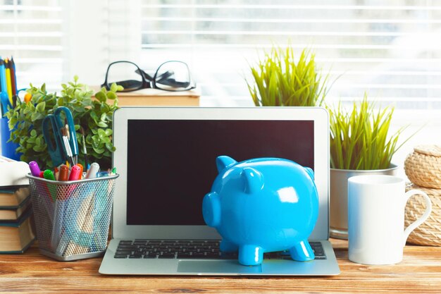 Piggy money box with laptop on wooden table