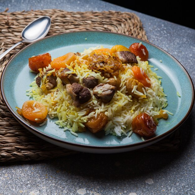 pilaf with meet and dried fruits and chestnut and spoon in round plate